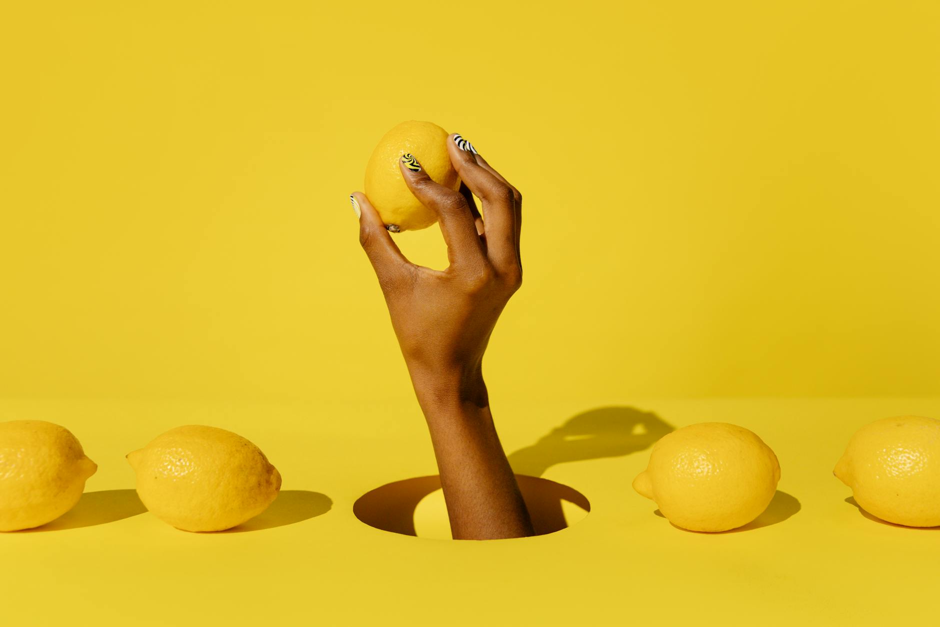 Eine Hand hält eine Zitrone vor leuchtend gelbem Hintergrund, symbolisiert Frische und weibliche Lust