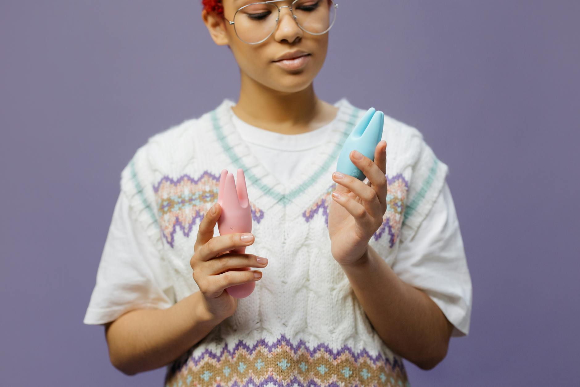 Frau mit Brille hält zwei farbige Vibratoren in nachdenklicher Pose